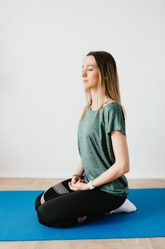 Side view of young slim female in sportswear sitting in Virasana pose with closed eyes while practicing yoga at home