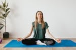 Serene blond lady in sportswear sitting with crossed legs and closed eyes while practicing yoga at home near potted plants