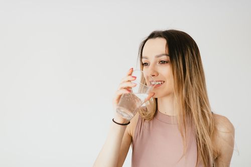 Free Optimistic young lady in top smiling while drinking glass of sparkling water and looking away Stock Photo
