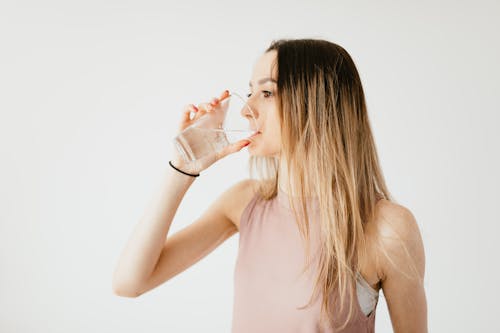 Young thirsty fit female with long hair in sportswear drinking water while recreating after workout