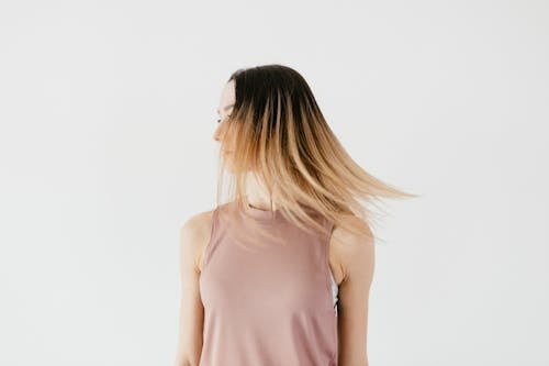 Free Serious unrecognizable young female in casual outfit with long loose hair hiding face standing against white background and looking away Stock Photo