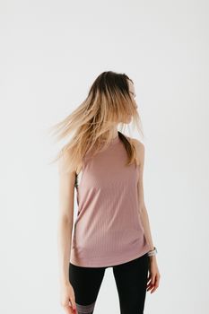 Anonymous young slim woman in sportswear with long hair covering face doing neck exercise during training in studio