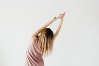 一位年轻女性在锻炼时伸展胸腔、举起手臂的匿名背影