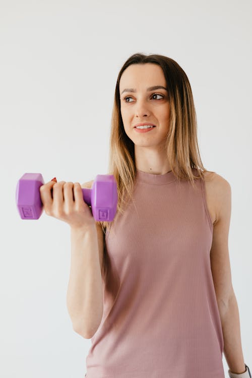 Free Cheerful young slim female athlete in comfy top holding dumbbell and looking away during fitness training Stock Photo