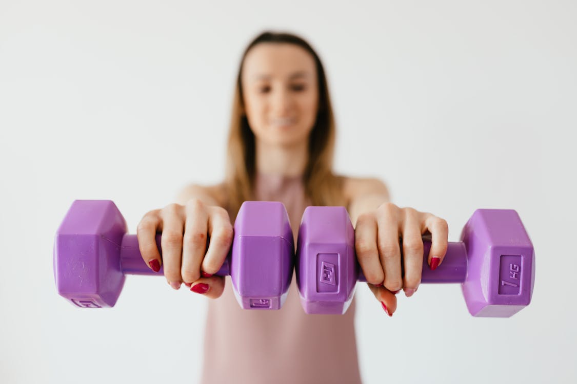 Free Defocused content young female doing bicep exercise with dumbbells during functional training in light studio Stock Photo