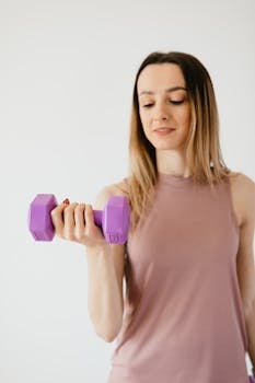 A young woman lifting a purple dumbbell during a fitness session in a studio.