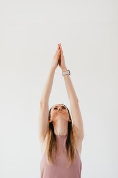 Slender young female in casual wear clasping hands while stretching in Urdhva Hastasana yoga position at home isolated on white background