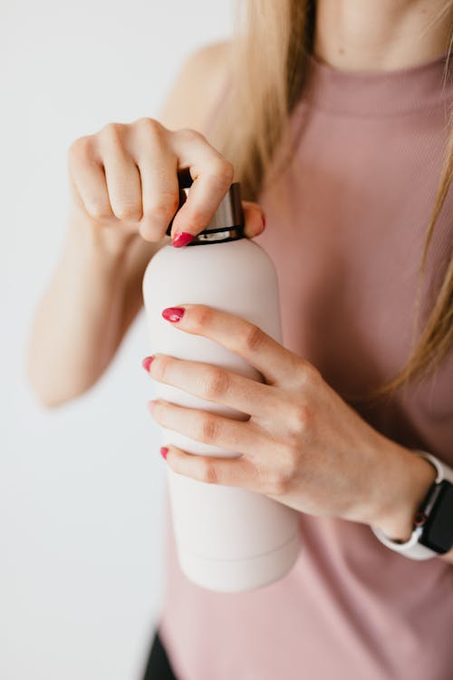 Unrecognizable woman with red nails opening cosmetic bottle against white background