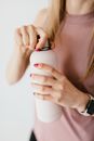 Unrecognizable woman with red nails opening cosmetic bottle against white background