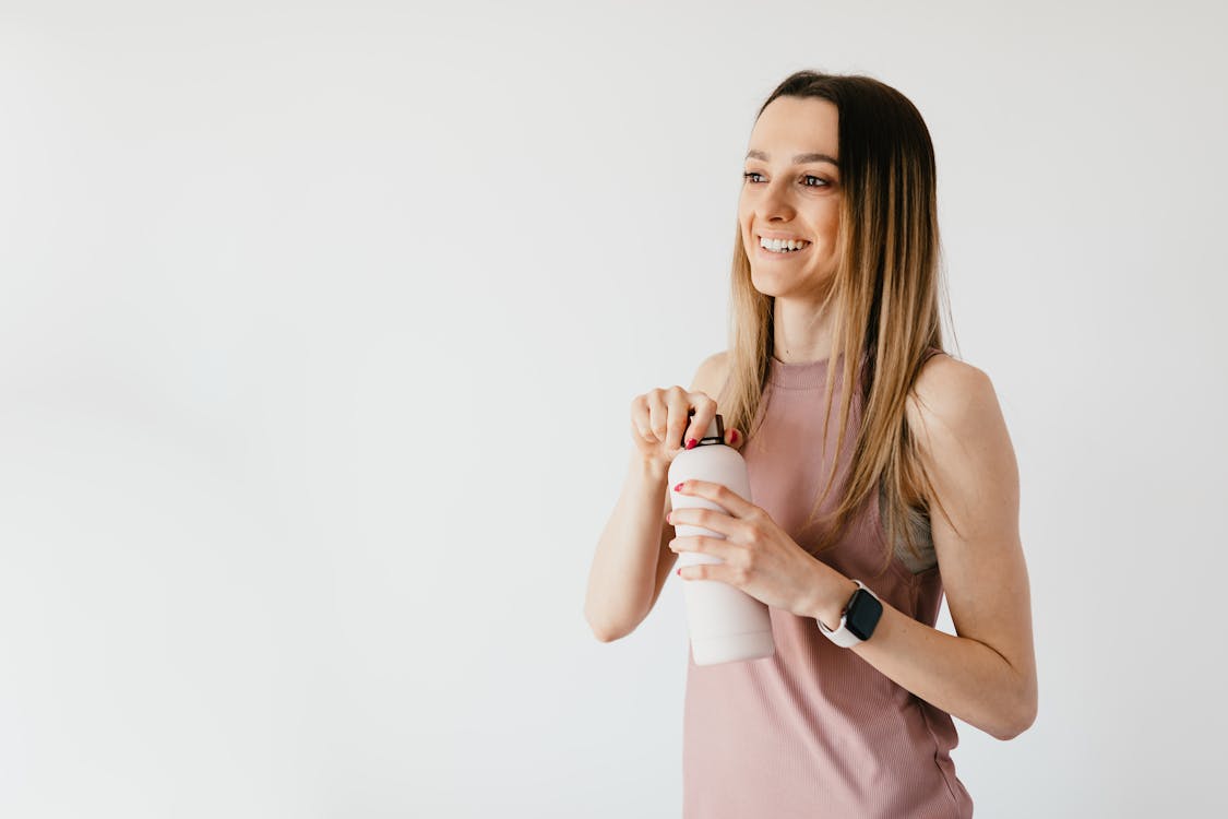Free Happy young woman opening cosmetic bottle while standing against white background Stock Photo