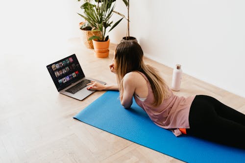 Young woman lying on floor on mat while using laptop at home