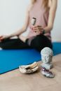 Selective focus of crop faceless young female in casual wear meditating in lotus pose with white sage incense near Buddha head sculpture amethyst crystal and palo santo wood in stone bowl