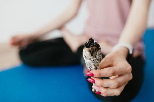 Free Anonymous female holding sage incense bundle while sitting in pose of lotus on rubber blue mat Stock Photo