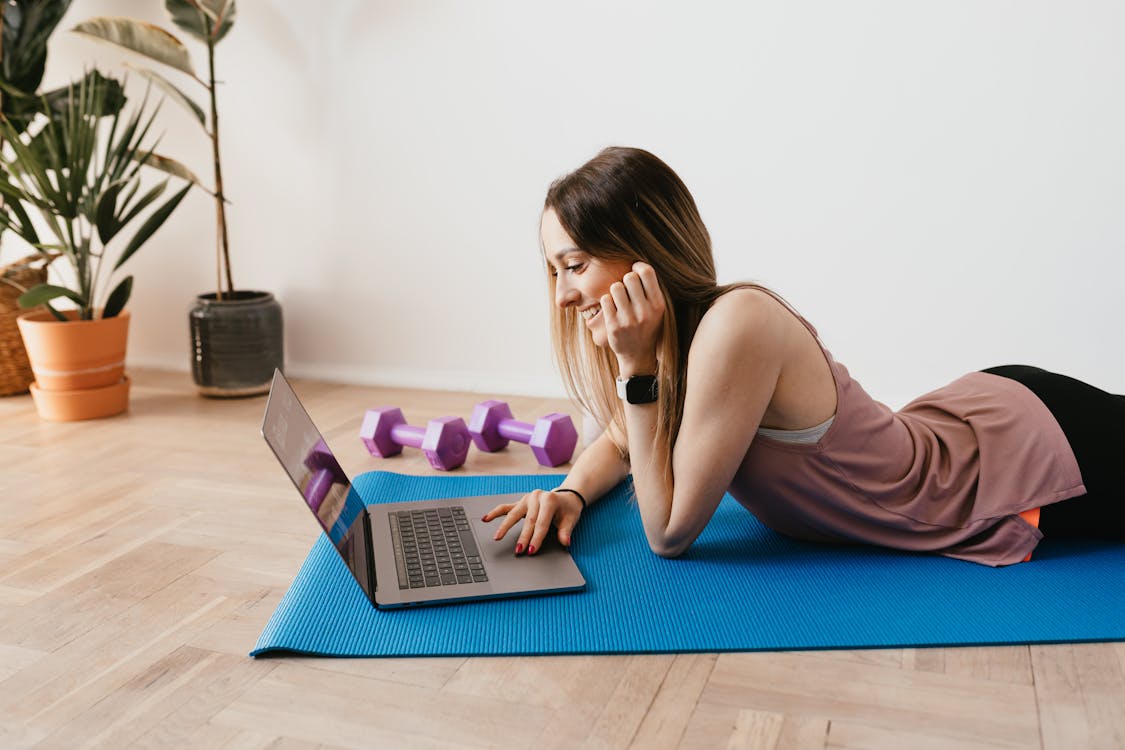 Slim woman browsing laptop on yoga mat · Free Stock Photo