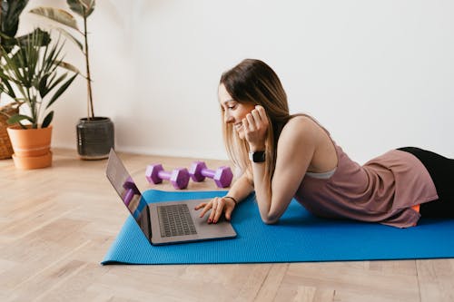 Free Side view of young happy slim female with long hair using laptop and smiling while lying on blue rubber mat Stock Photo