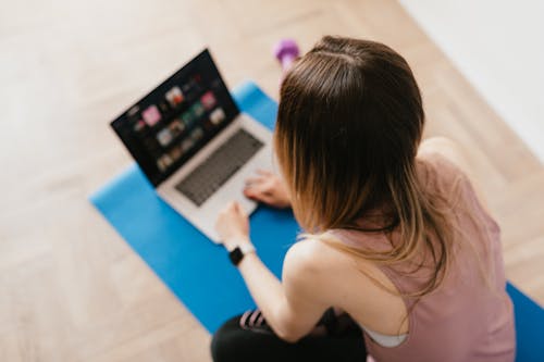 Woman sitting on mat and surfing internet on laptop