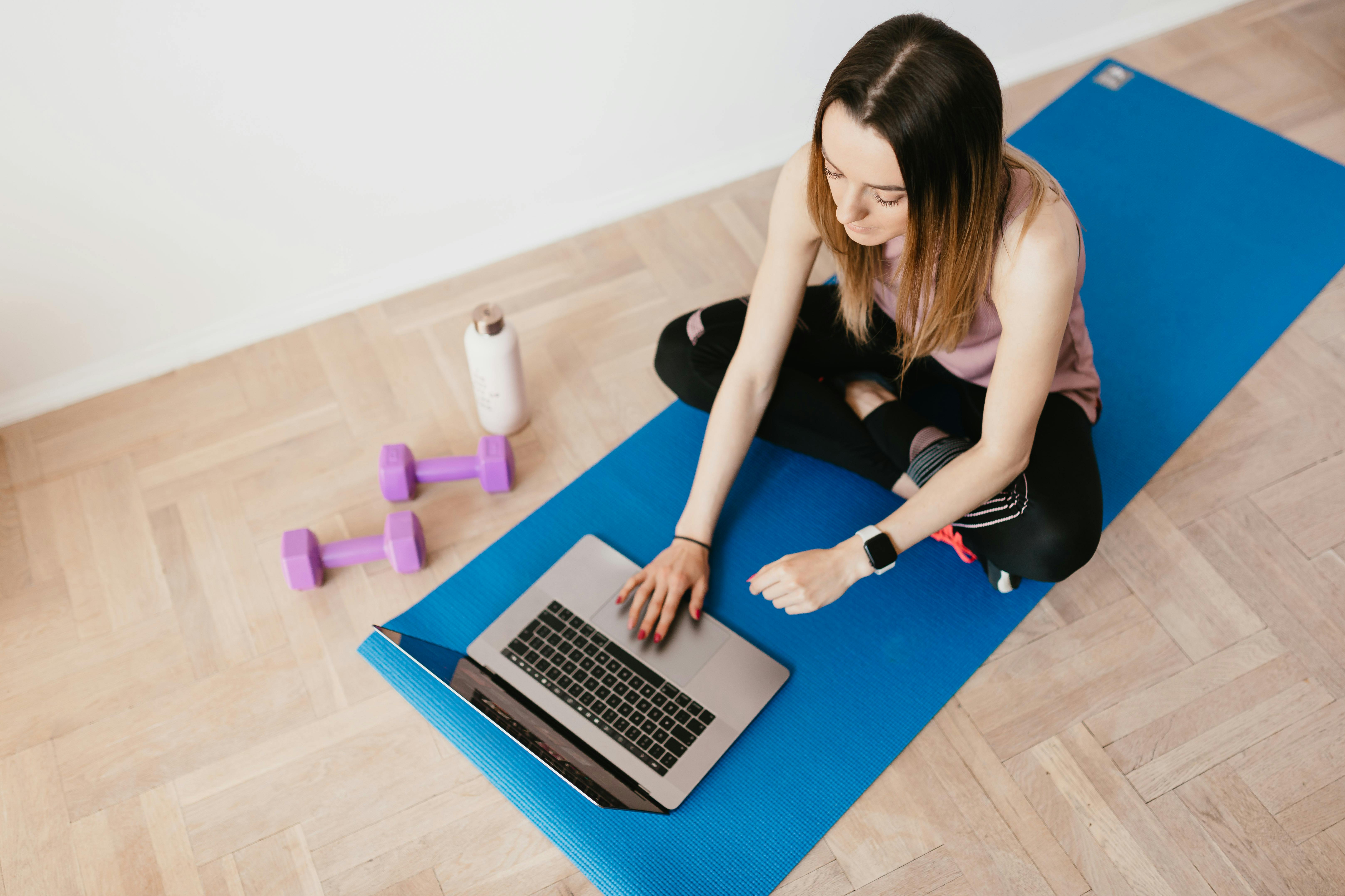 young woman with laptop sitting on yoga mat