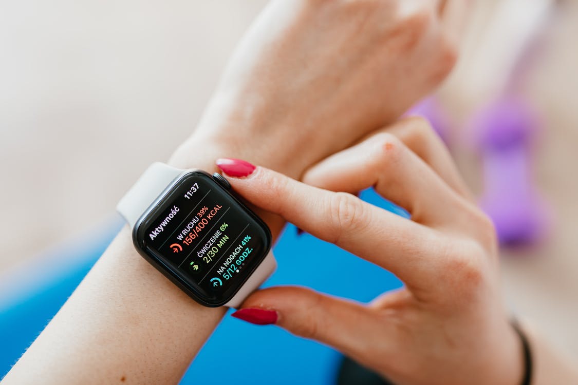 Unrecognizable female with manicure checking smartwatch on hand while sitting on yoga mat