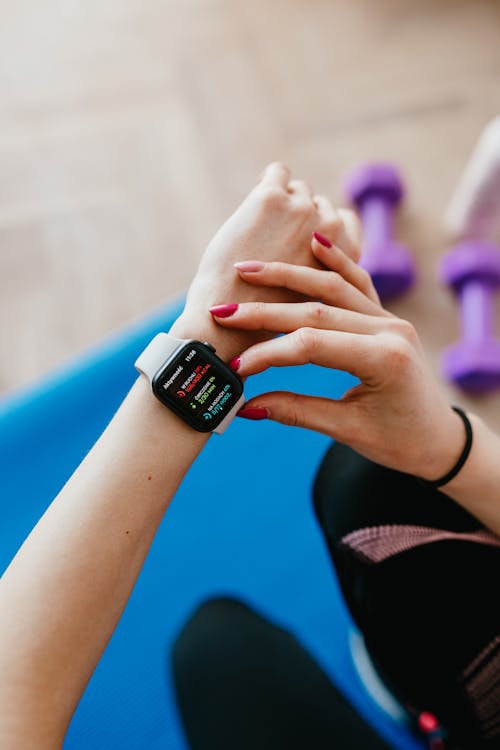 Free Unrecognizable female in sportswear sitting on yoga mat and looking at smart watch on hand Stock Photo