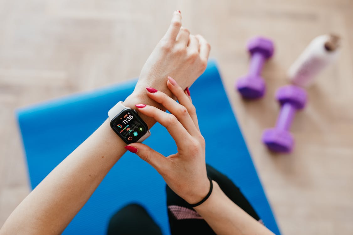 Free Anonymous sportswoman checking smart watch and sitting on mat Stock Photo