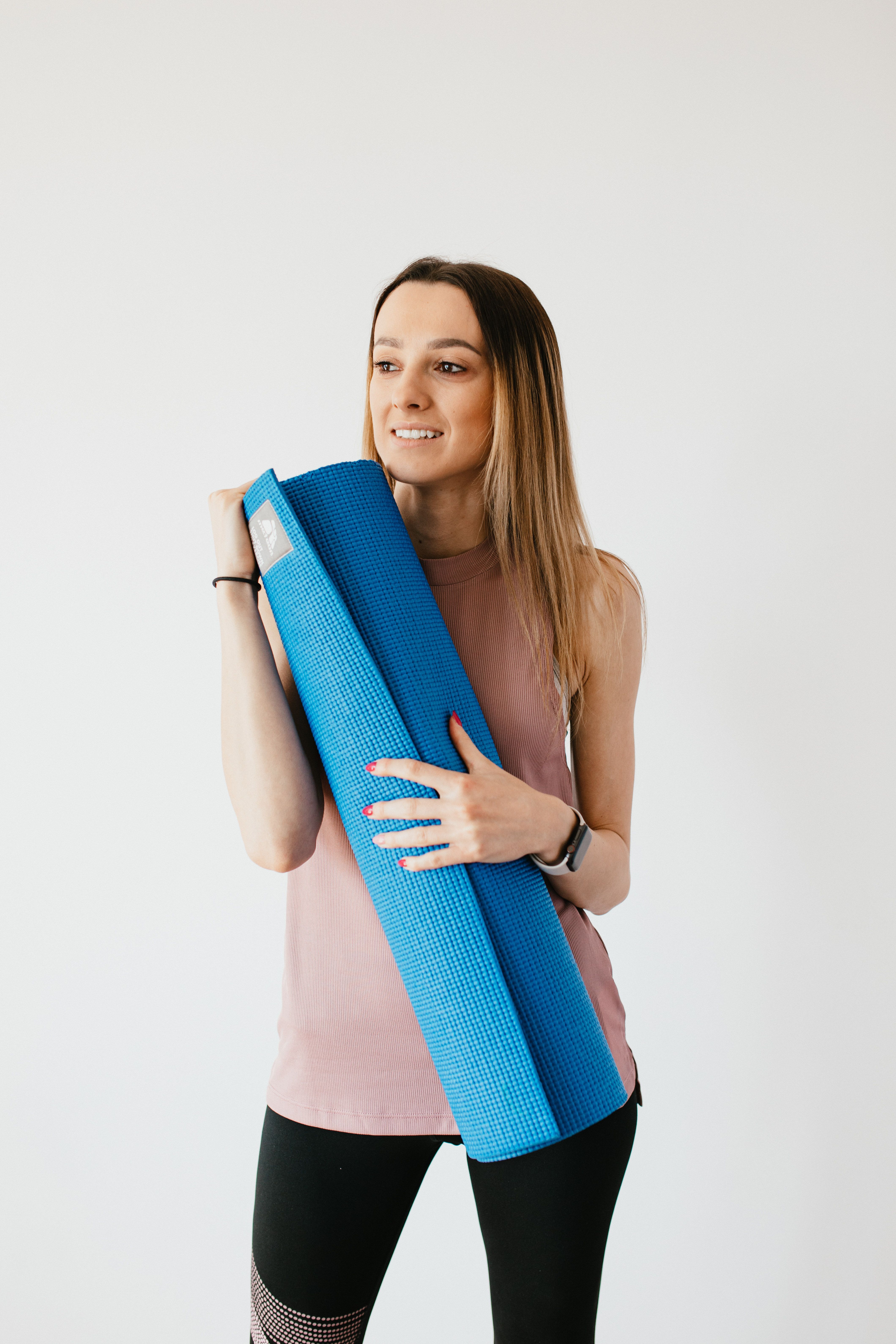 Young woman with yoga mat standing near gray wall