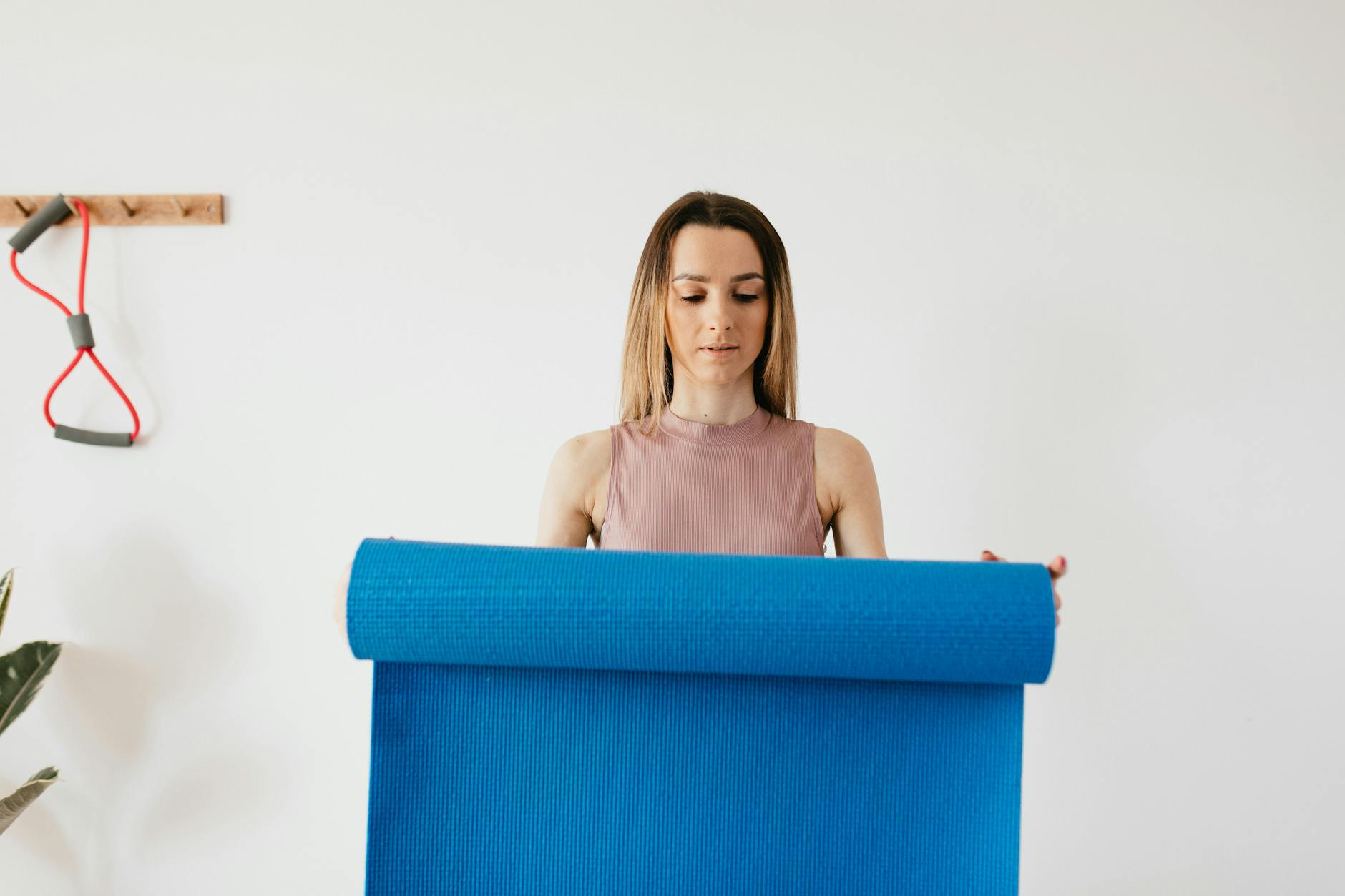 Serious young female in sportswear standing near gray wall with blue yoga mat in hands