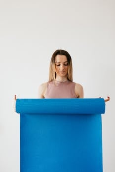 Young woman unfolding a blue yoga mat indoors, focusing on preparation.