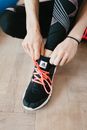 From above young anonymous female athlete in leggings adjusting sneakers while sitting on wooden floor in modern fitness studio and preparing for training