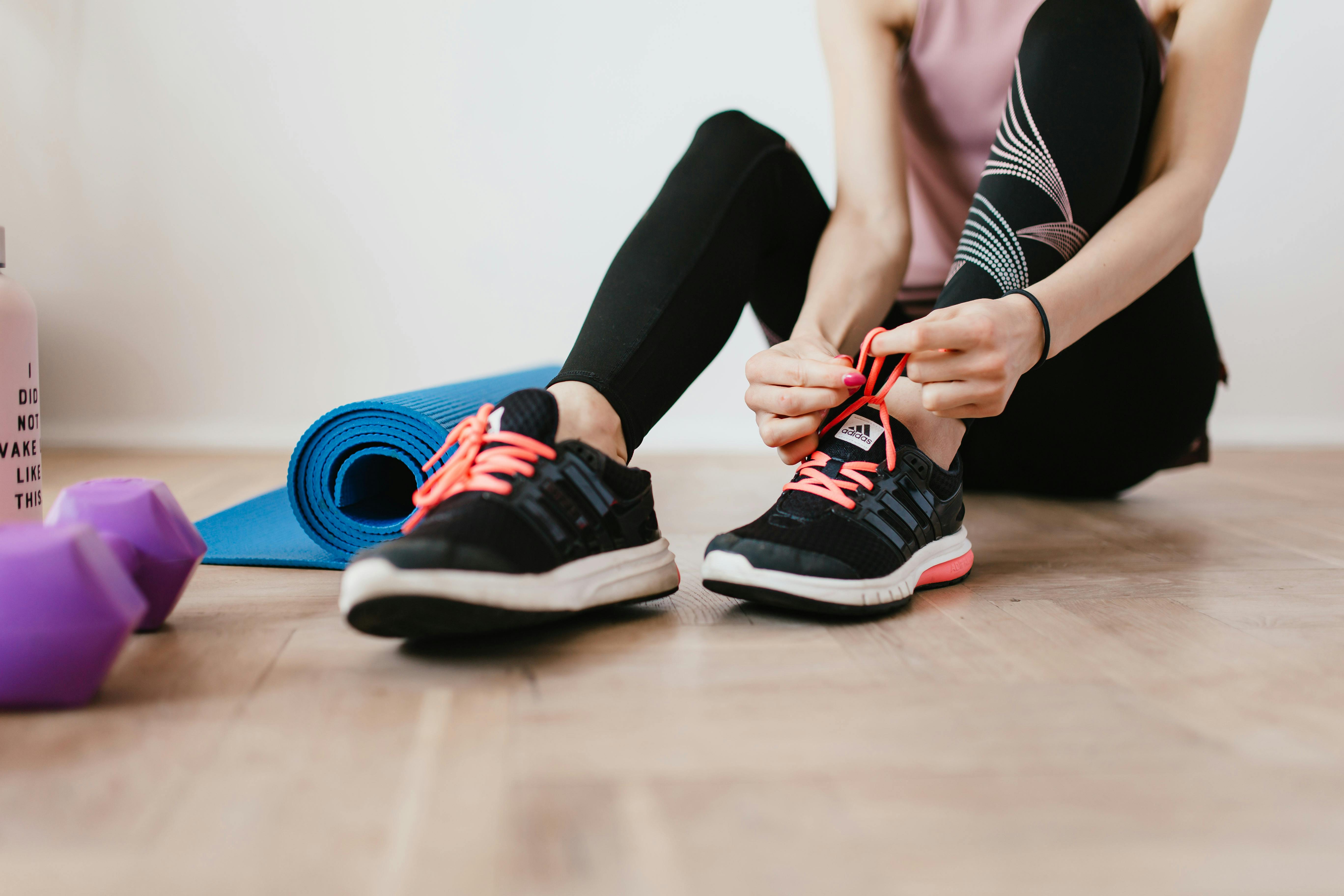 anonymous slender female athlete tying shoelaces near sport accessories