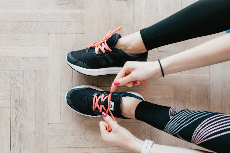 Unrecognizable Young Sportswoman Tying Sneakers On Floor