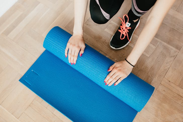 Crop young sportswoman unfolding blue yoga mat