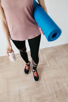 一位女性在室内准备瑜伽课程，手里拿着垫子和水瓶