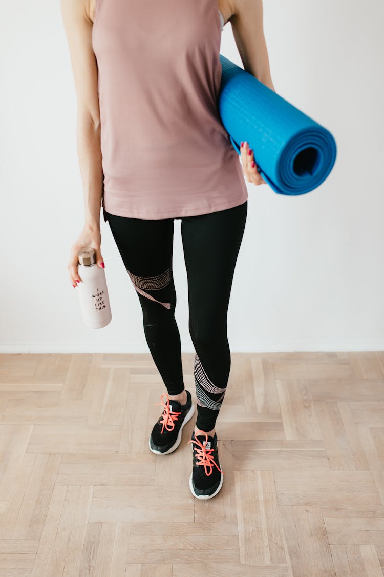 Unrecognizable Sportswoman Carrying Sport Mat And Bottle Of Water Before Indoors Training