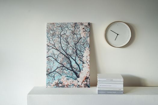 一幅静物画宁静地呈现，白色的桌子上摆放着一幅树画、一个时钟和一些书籍