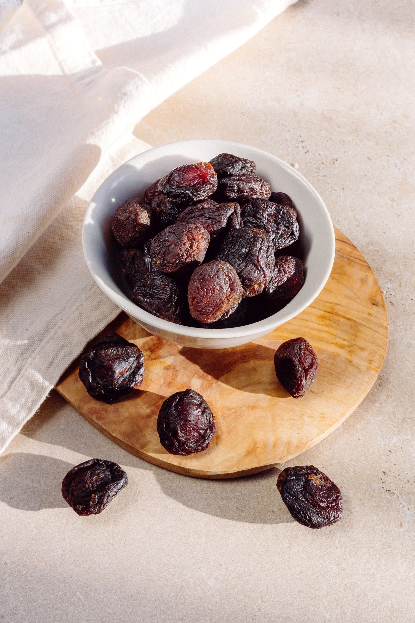 Whole dried prunes in a white bowl on a wooden board