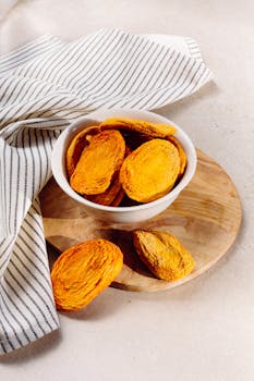 Vibrant dried apricots in a white bowl on wooden board with striped cloth.
