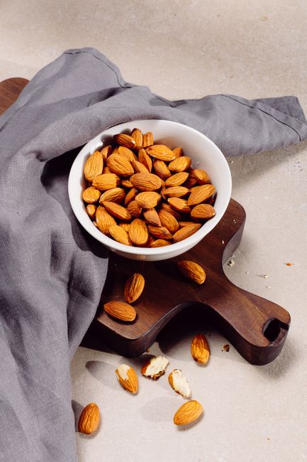 A bowl of almonds on a wooden board with scattered nuts for healthy snacking. - Price Comparison of Different Brands and Types of Snacks
