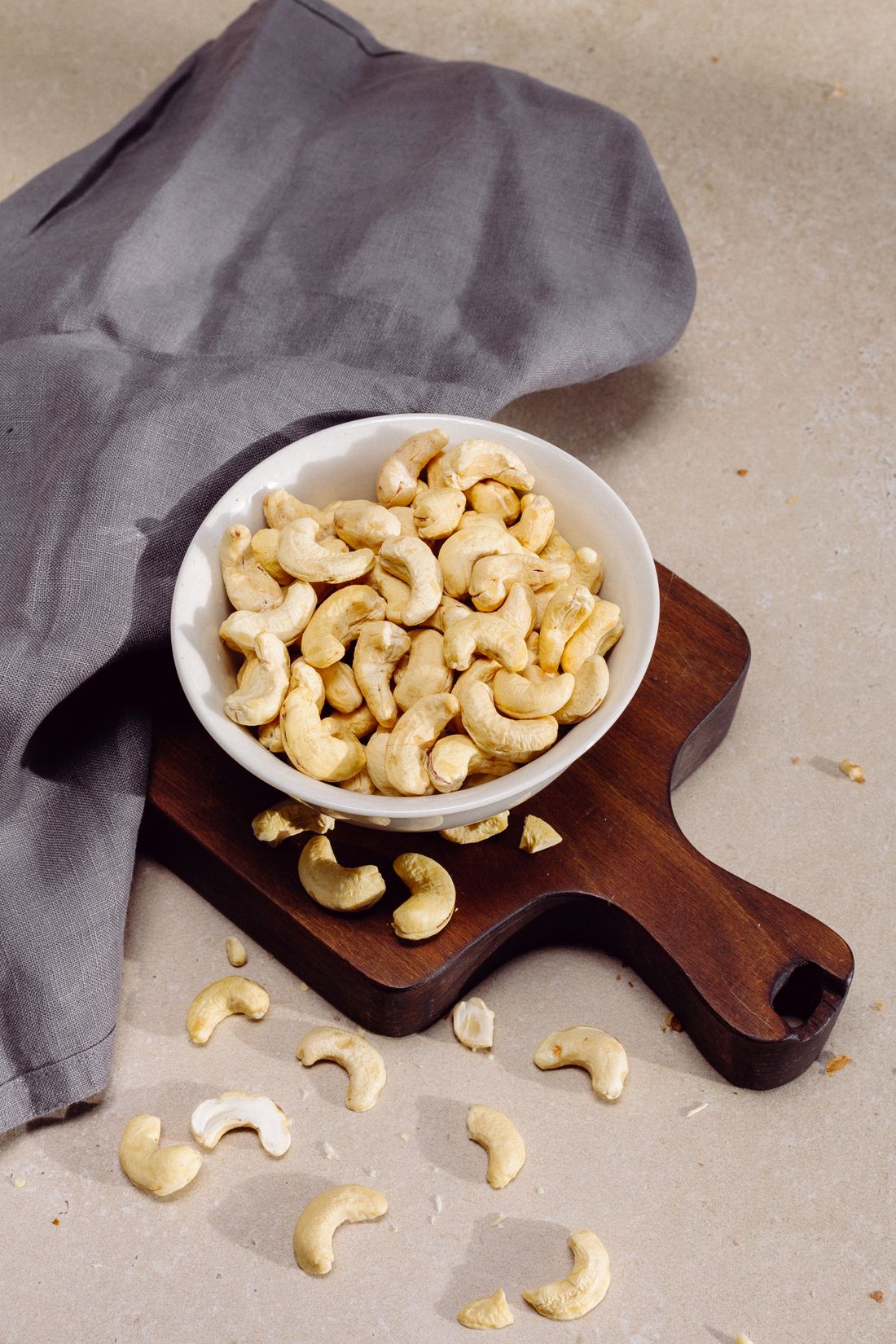 Whole cashews in a white bowl on a board