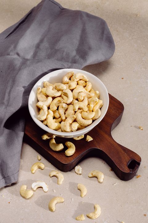 Whole cashews in a white bowl on a board