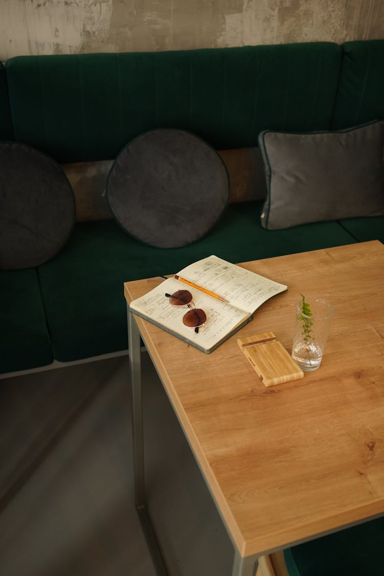 A Wooden Table With Notebook And Sunglasses Near The Couch