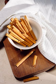 A top view of cinnamon sticks in a bowl on a wooden board with a napkin, creating a warm and inviting still life.
