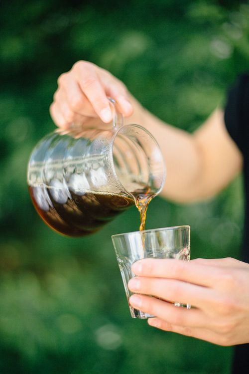 Free A detailed view of coffee being poured from a glass pitcher into a glass cup outdoors. Stock Photo
