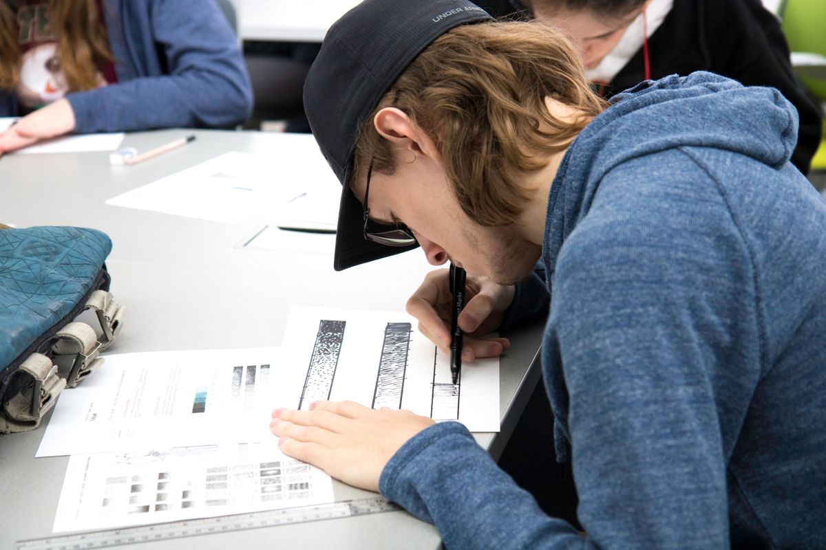 Young adult studying art by drawing detailed pencil sketches in a classroom