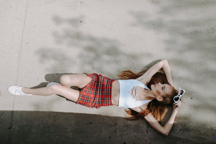 Woman In White Halter Top And Red Plaid Skirt Lying On Concrete Pavement