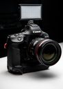 Rectangular flash placed on top of black photo camera placed on white table against dark wall in modern studio room