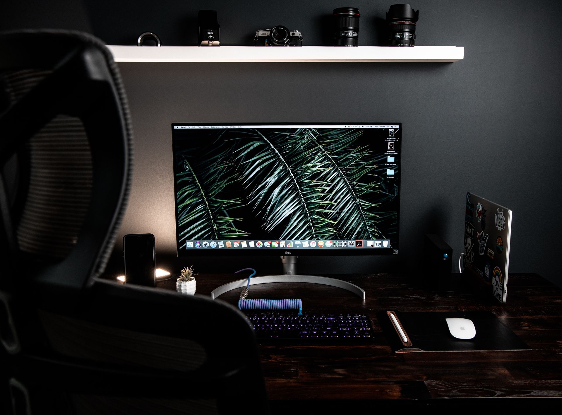 Contemporary home office setup with computer monitor, keyboard, and tech devices on a dark desk.