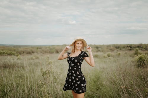 Woman in Black Floral Dress With Sunhat Standing on Grass Field