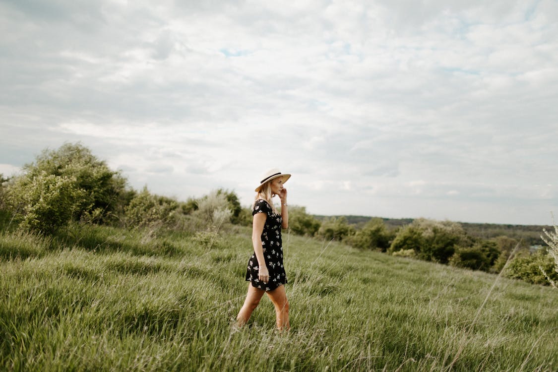 Woman in Black and White Floral Dress Walking on Green Grass Field