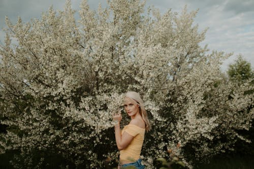 Woman in Yellow Off Shoulder Shirt Standing Near A Blooming Tree