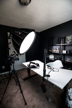 Modern lamp on tripod placed near lighting devices illuminating desk with chair and shelves with frames in small cozy room